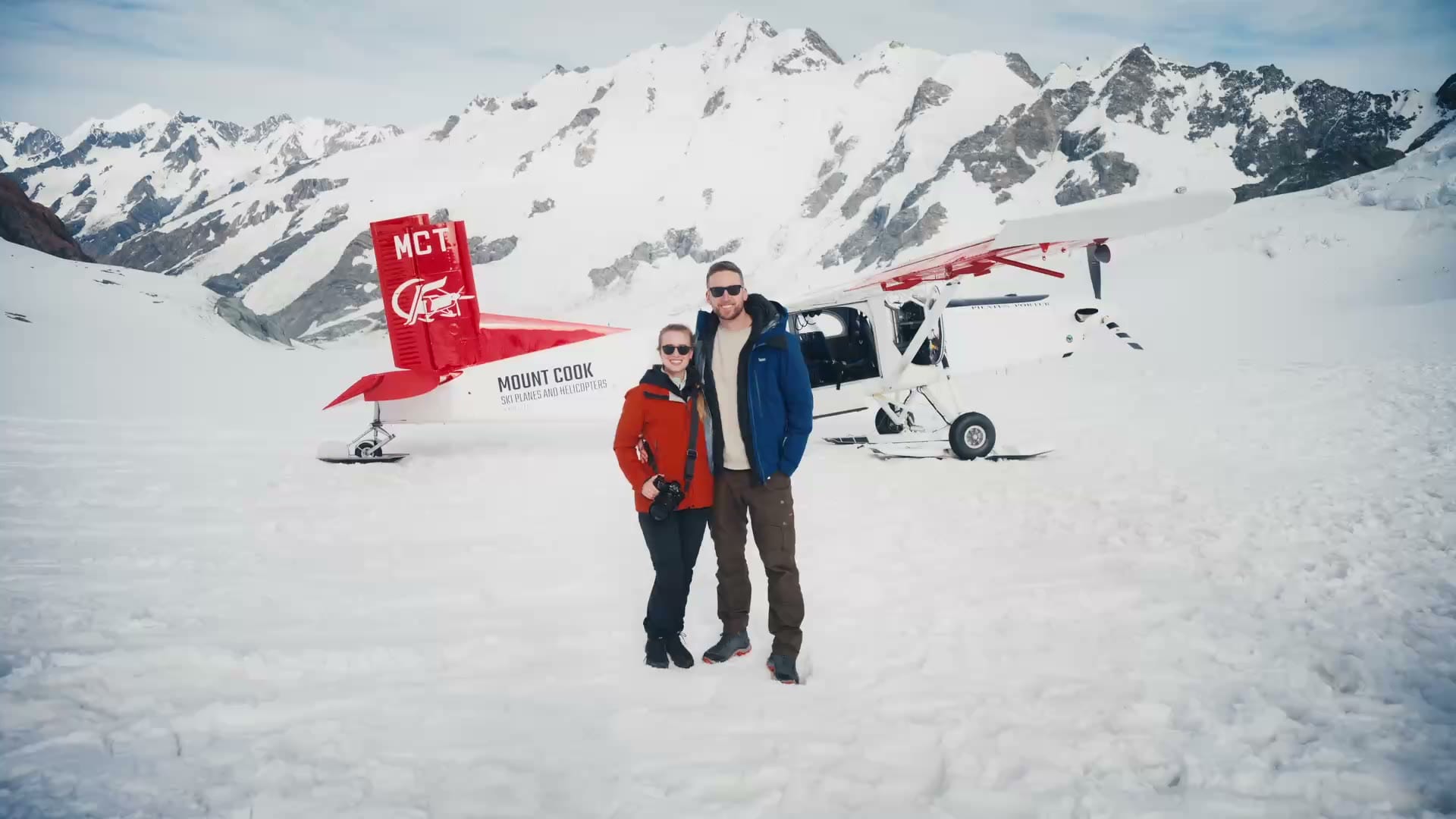 Two travellers beside a ski plane in a snowy mountain landscape