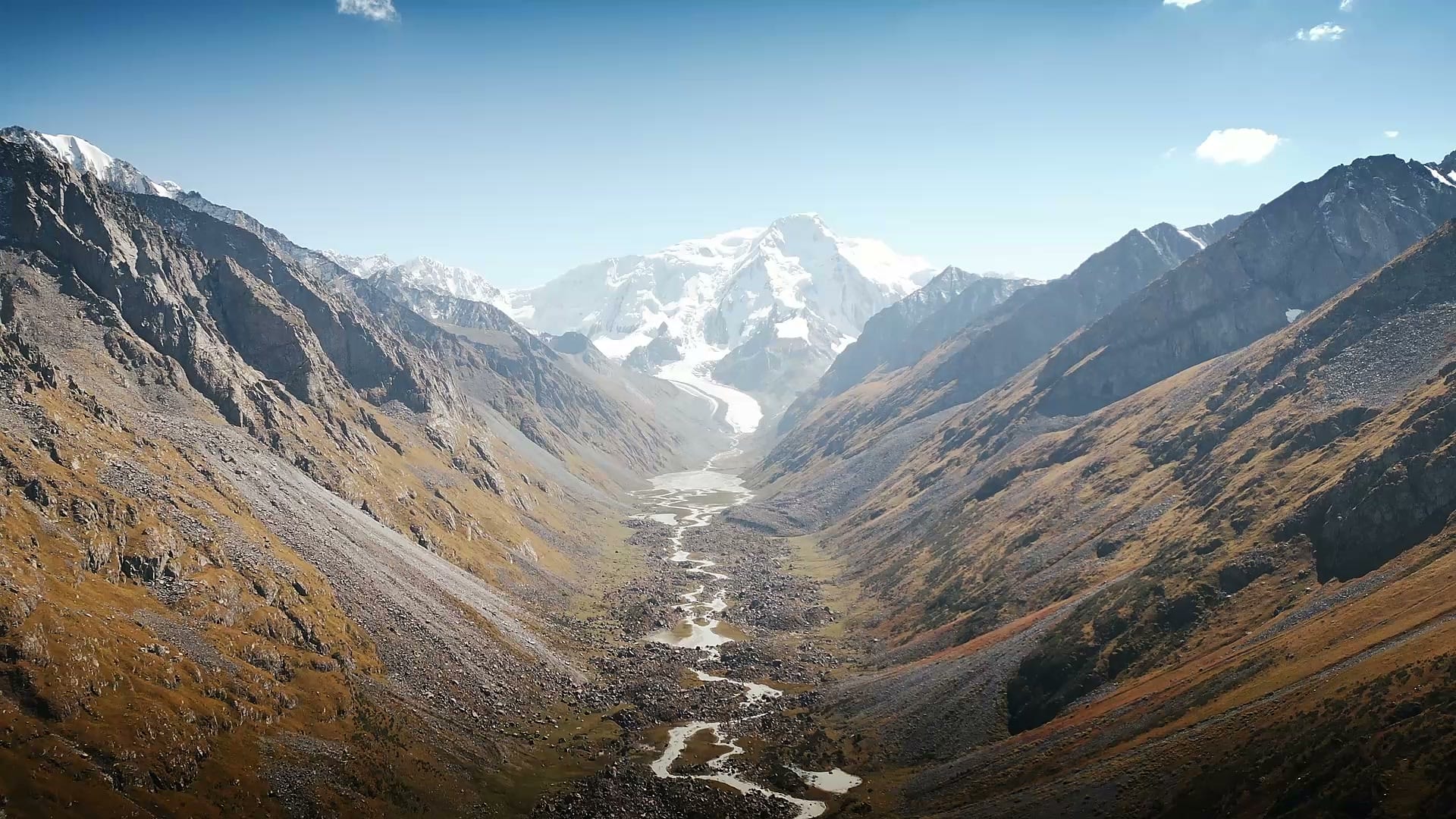 Glacier and snow-covered mountain above a rocky valley with winding meltwater streams